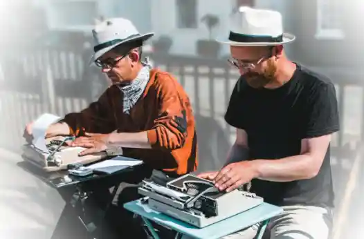 Two men in white hats writing on typewriters